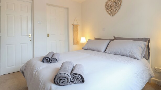 A bedroom with a bed, two doors, a wall-mounted heart decoration, and a bedside lamp.