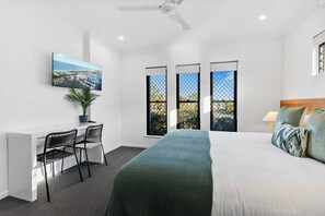 A bedroom with a bed, a desk, two chairs, a TV, and a window with a view of the city.