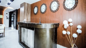 A reception area with a wooden wall, three clocks, a reception desk, and a decorative plant. - Underskies Spa and Hotel (Parañaque)