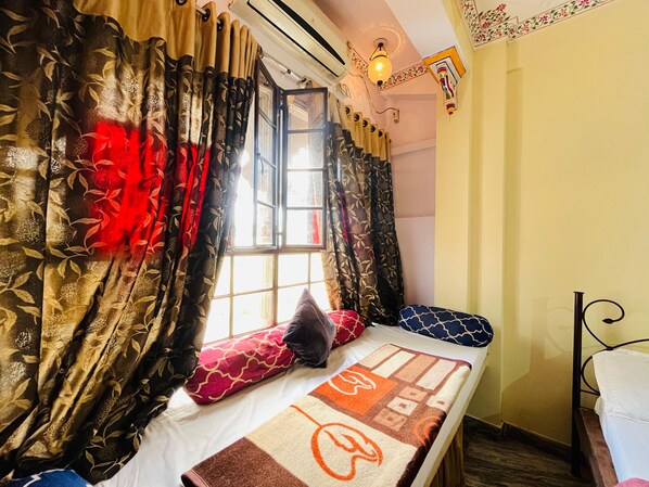 A room with a bed, a window with curtains, and a wall-mounted light fixture. - Hotel Heritage haveli (Udaipur)