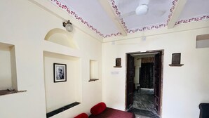 A room with a bed, a wall-mounted shelf, a framed picture, and a door leading to another room. - Hotel Heritage haveli (Udaipur)