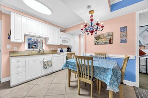 Una cocina con armarios blancos, una mesa de comedor cubierta con mantel azul y una lámpara de araña.