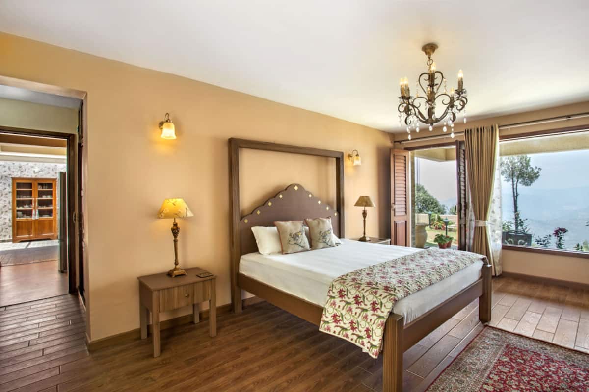 Quarto com cama de madeira, abajures, um candelabro e vista para o exterior.