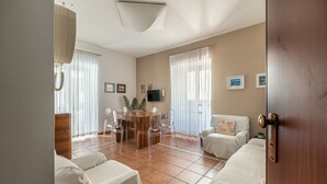 A spacious living room with a round dining table, clear chairs, a sofa, and a TV mounted on the wall.