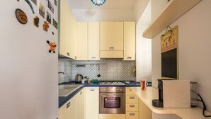 A compact kitchen with light yellow cabinets, a stainless steel oven, and a coffee maker on the counter.