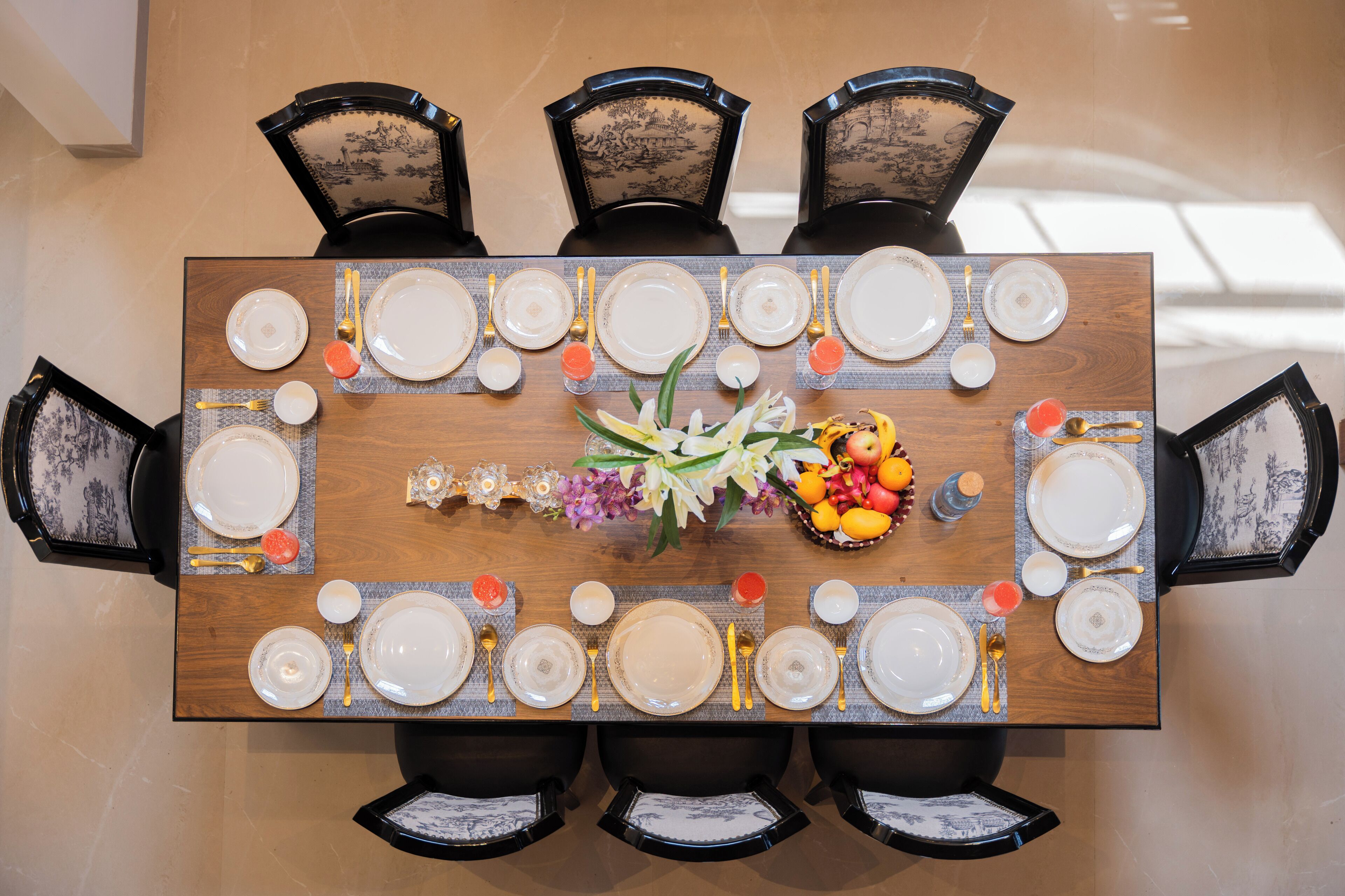 A rectangular dining table set for six with a floral centerpiece and fruit basket.