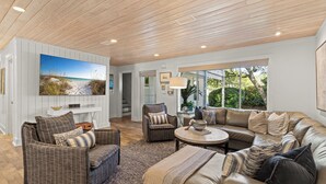 A spacious living room with a large sectional sofa, a smaller sofa, and a round coffee table. There is a flat-screen TV mounted on the wall, and the room has wooden flooring and a high ceiling. - "3 By The Sea" | Large Pool, 6 Bikes & 30A Charm, Steps to Beach Access (Santa Rosa Beach)