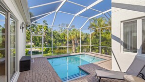A covered outdoor swimming pool with a clear view of a lake and palm trees.