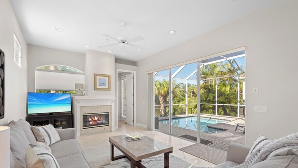 A modern living room with a fireplace, a flat-screen TV, and a large sliding glass door leading to a pool area.