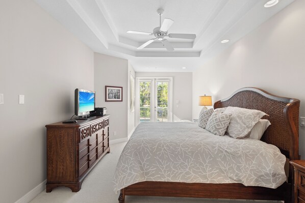 A bedroom with a bed, a dresser, a television, and a ceiling fan.