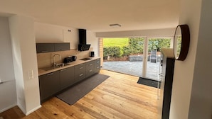 Een moderne keuken met een groot eiland, inbouwapparatuur en een schuifpui naar een terras.