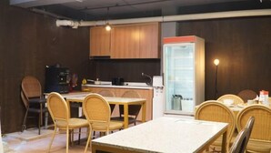 A modern kitchen with wooden cabinets, a refrigerator, and a dining area with wicker chairs and a marble table. - Kumho Ryokan for Female Travelers – Near Dongdaemun (Seoul)