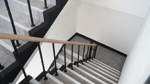 A staircase with black railings and a wooden handrail, leading to a landing with a striped carpet. - Kumho Ryokan for Female Travelers – Near Dongdaemun (Seoul)