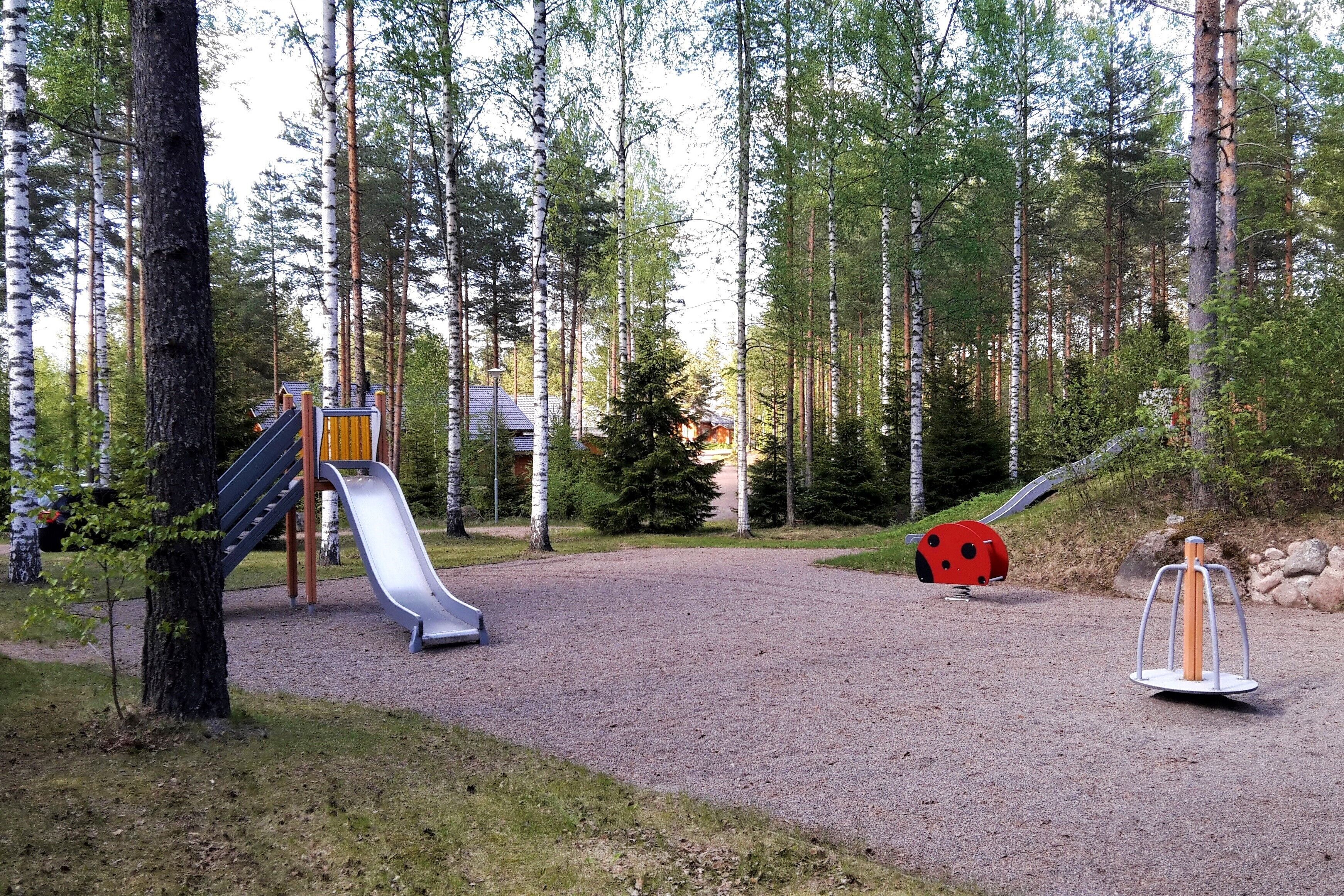 A playground with a slide and a swing set in a forested area.