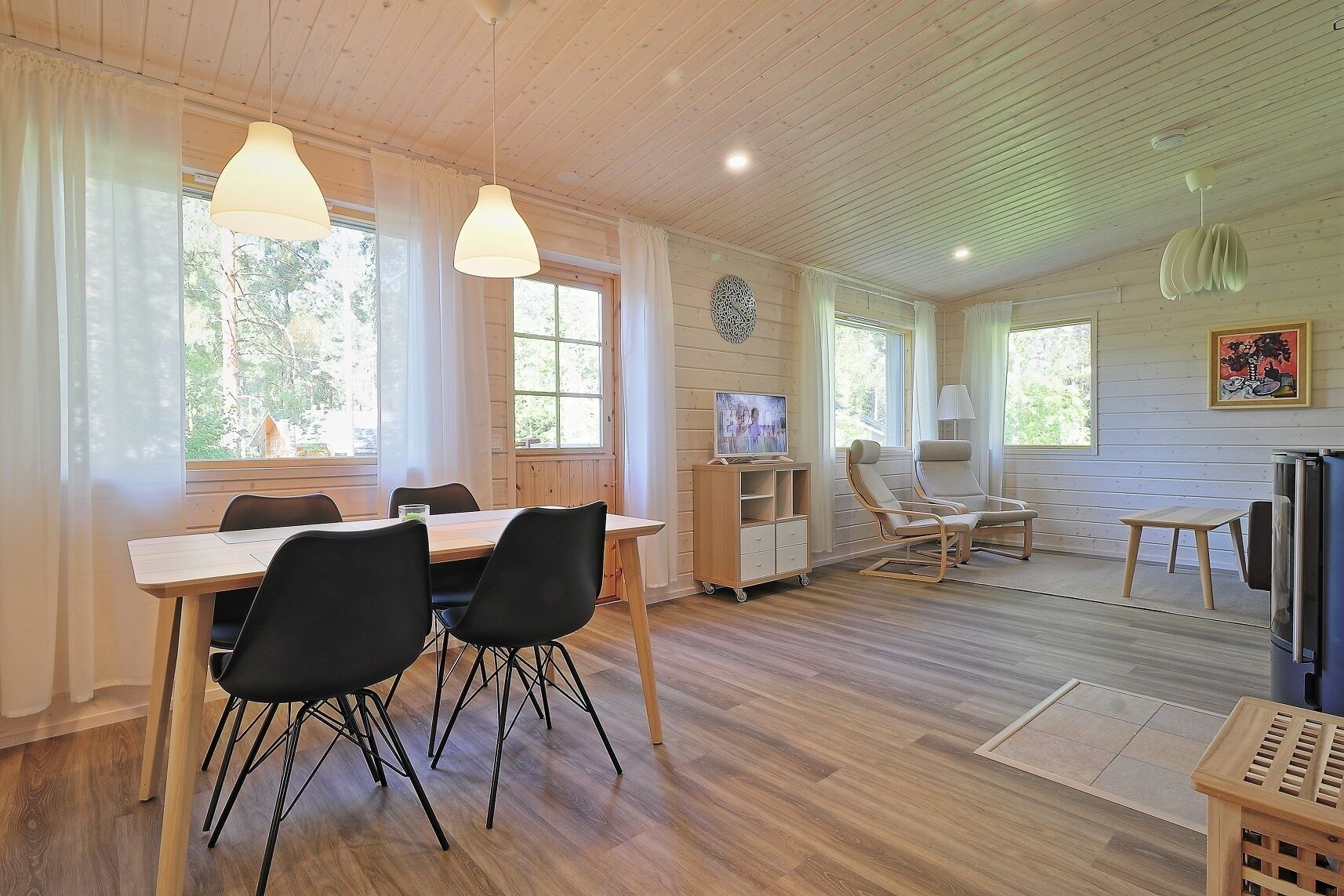 Un interior moderno con una mesa de comedor de madera, sillas negras, un televisor y un espacio de estar con sofá y sillones.