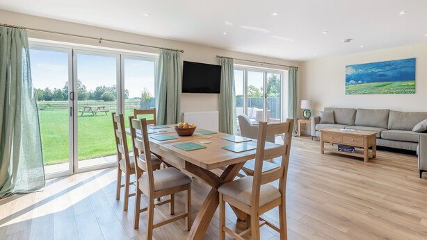 A spacious living area with a dining table, chairs, a sofa, and a TV mounted on the wall.