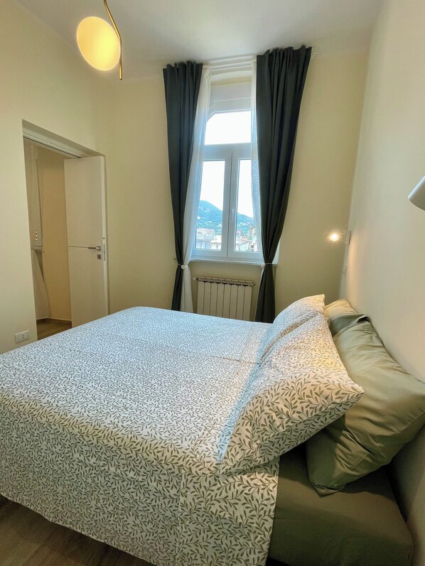 Quarto com cama, janela com cortinas, radiador e porta.