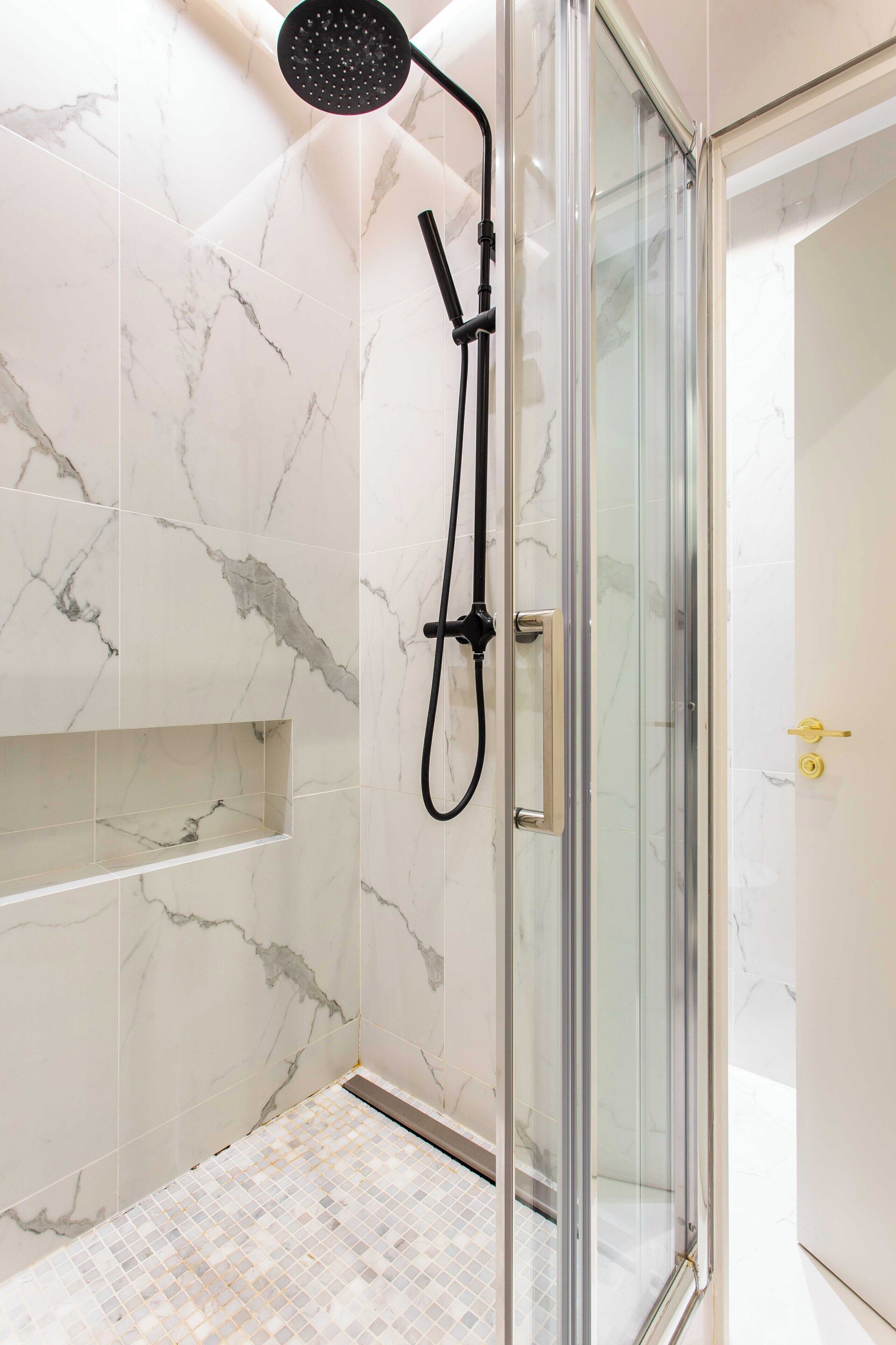 Una cabina doccia in vetro con soffione a mano, pareti in marmo e pavimento piastrellato.