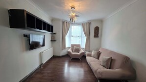A living room with a flat-screen TV, a sofa, a chair, a radiator, and a ceiling light fixture.