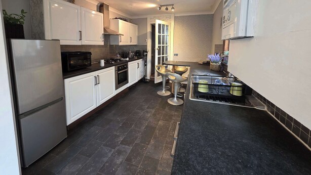 A compact kitchen with white cabinets, a stainless steel refrigerator, a gas stove, and a dining area with two chairs.