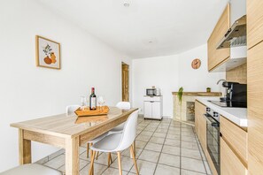 A modern kitchen with wooden cabinets, a dining table with chairs, a microwave, and a clock on the wall.
