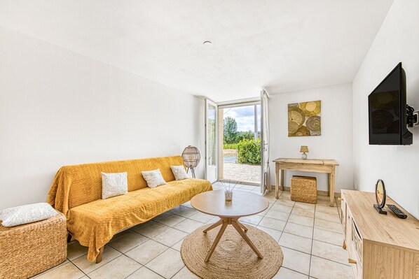 A room with a sofa, a round table, a wooden desk, a television, and a view through a glass door.