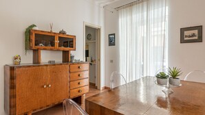 Un comedor con mesa de madera, sillas, un armario con puertas de cristal y una ventana con cortinas.