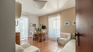 Amplia sala de estar con una mesa de comedor redonda, sillas transparentes, un sofá y un televisor montado en la pared.