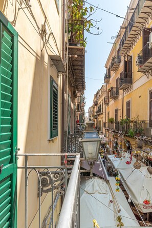 Una calle estrecha flanqueada por edificios, con balcones adornados con plantas y un farol.