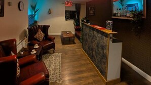 Una sala de estar acogedora con suelo de madera, sillones de cuero, una mesa de centro y una zona de bar con mostrador y estanterías.