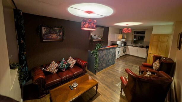 Una sala de estar con sofá, sillones, una mesa de centro y una cocina al fondo.