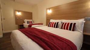 Habitación de hotel con dos camas, cada una con ropa blanca y almohadas a rayas rojas, y cabeceros de madera.