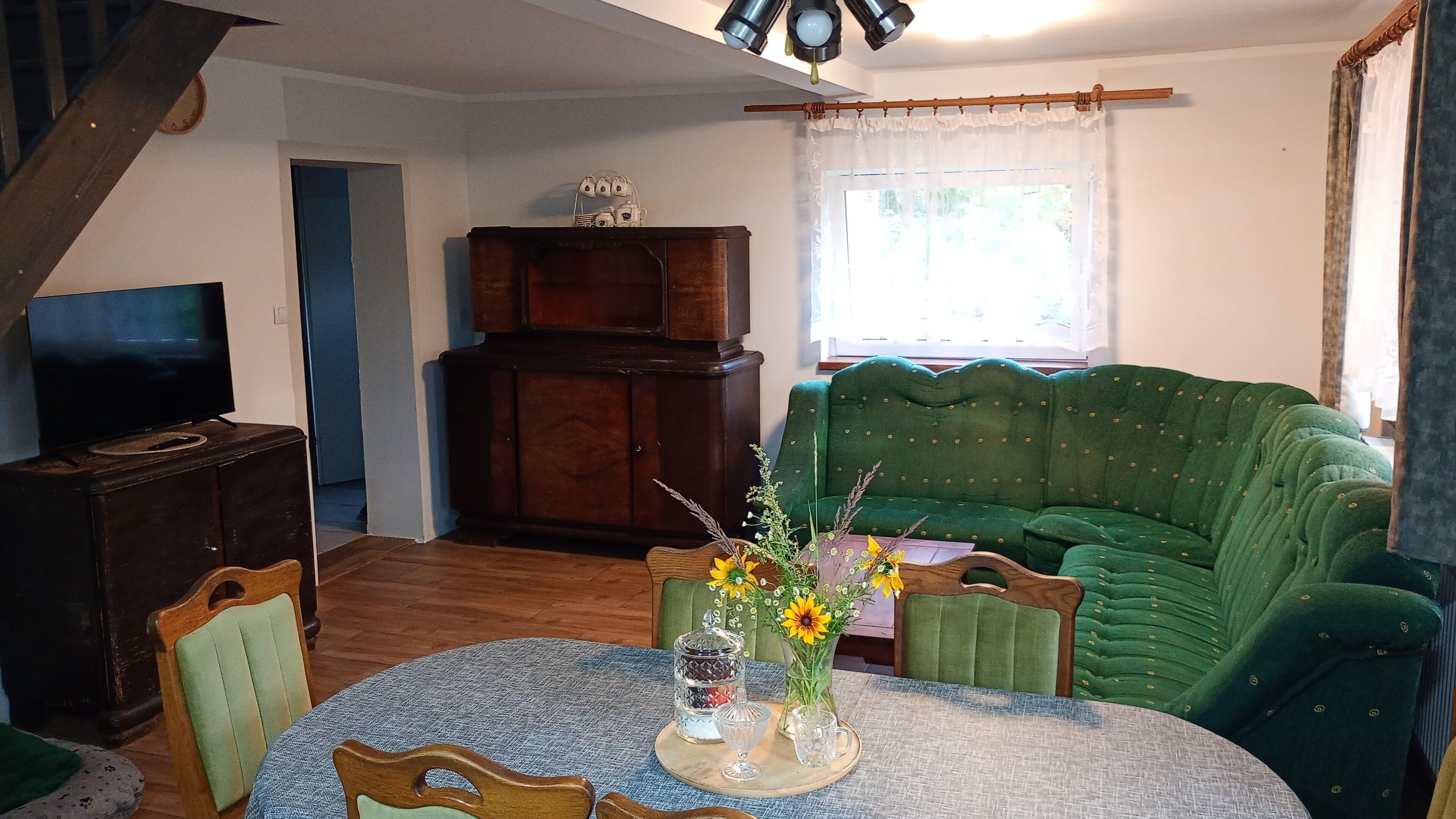 A cozy living room with a green sofa, a wooden cabinet, a television, and a dining table with chairs.