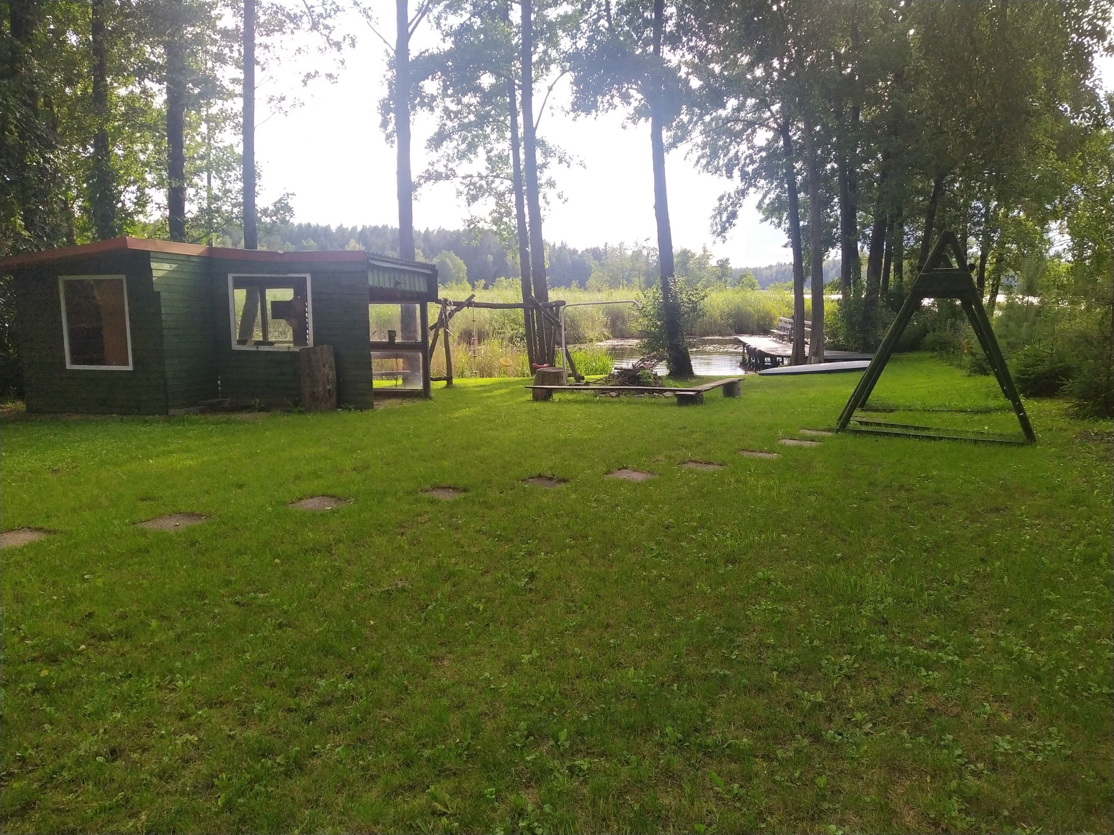 A grassy outdoor area with a small wooden structure, a swing set, and a pond.