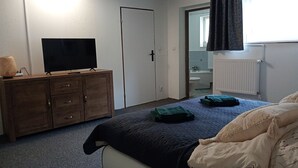 A bedroom with a bed, a dresser, a television, and a bathroom visible through an open door.