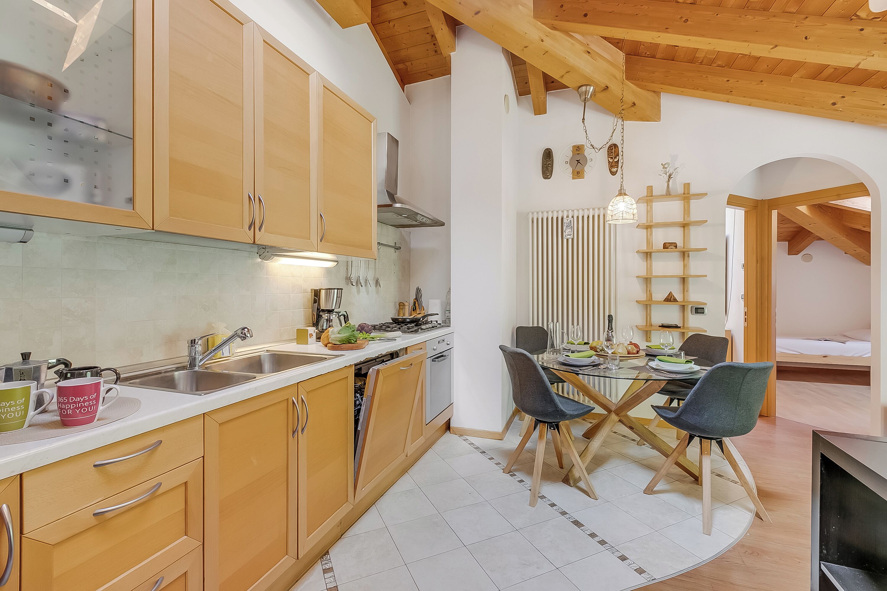 Una cocina moderna con armarios de madera, un comedor con mesa de vidrio y un espacio de sala de estar acogedor con una cama.