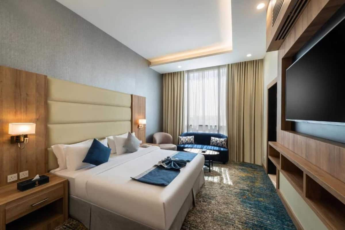A hotel room with a large bed, a sofa, a TV, and a desk.