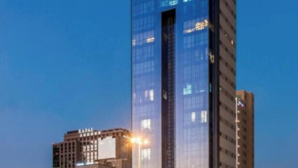 Ein Hochhaus mit Glasfassade, vermutlich ein Hotel oder Bürogebäude, mit beleuchteten Fenstern und blauem Himmel im Hintergrund.