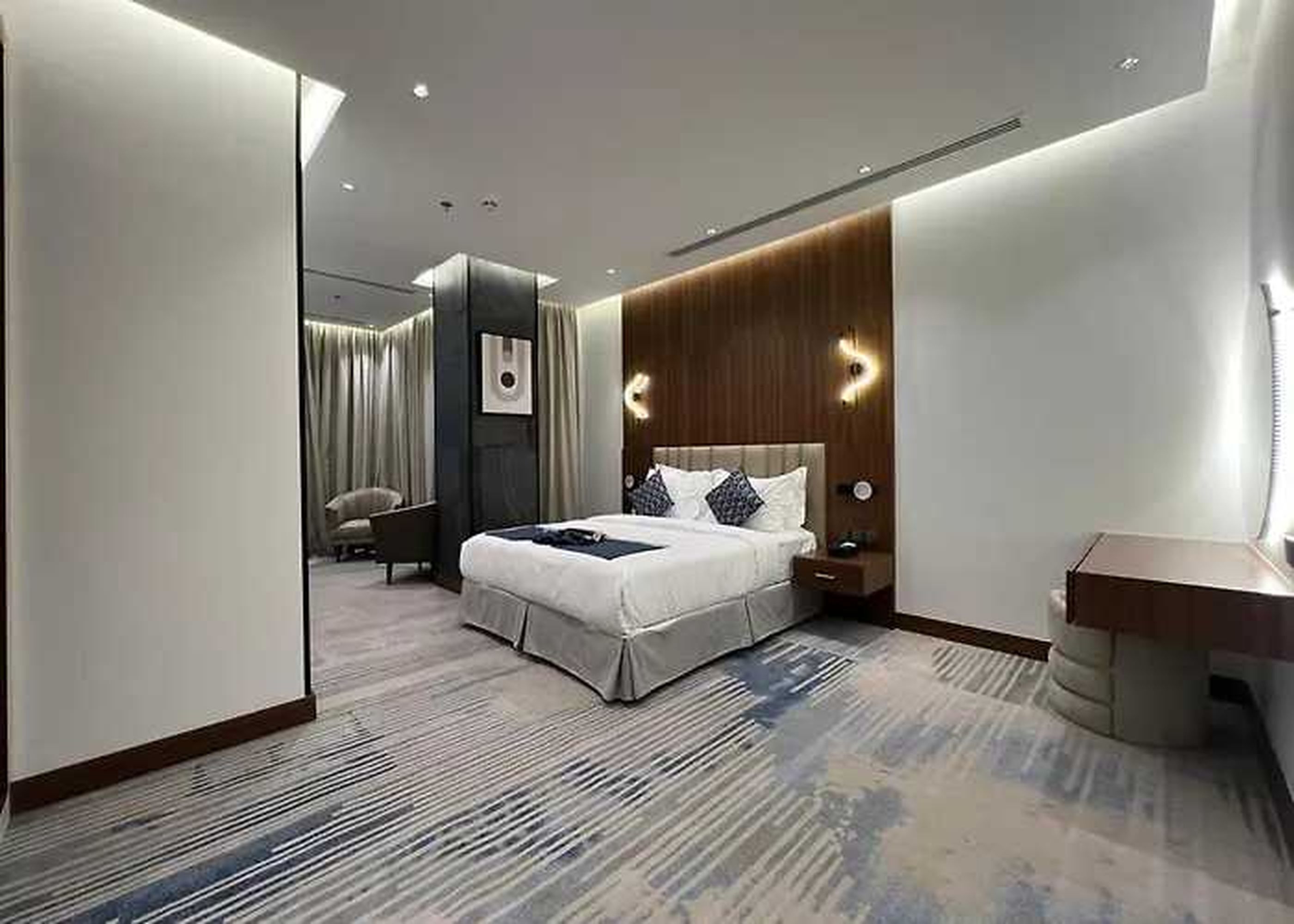 Een moderne hotelkamer met een groot bed, een houten hoofdbord, een nachtkastje en een stoel.