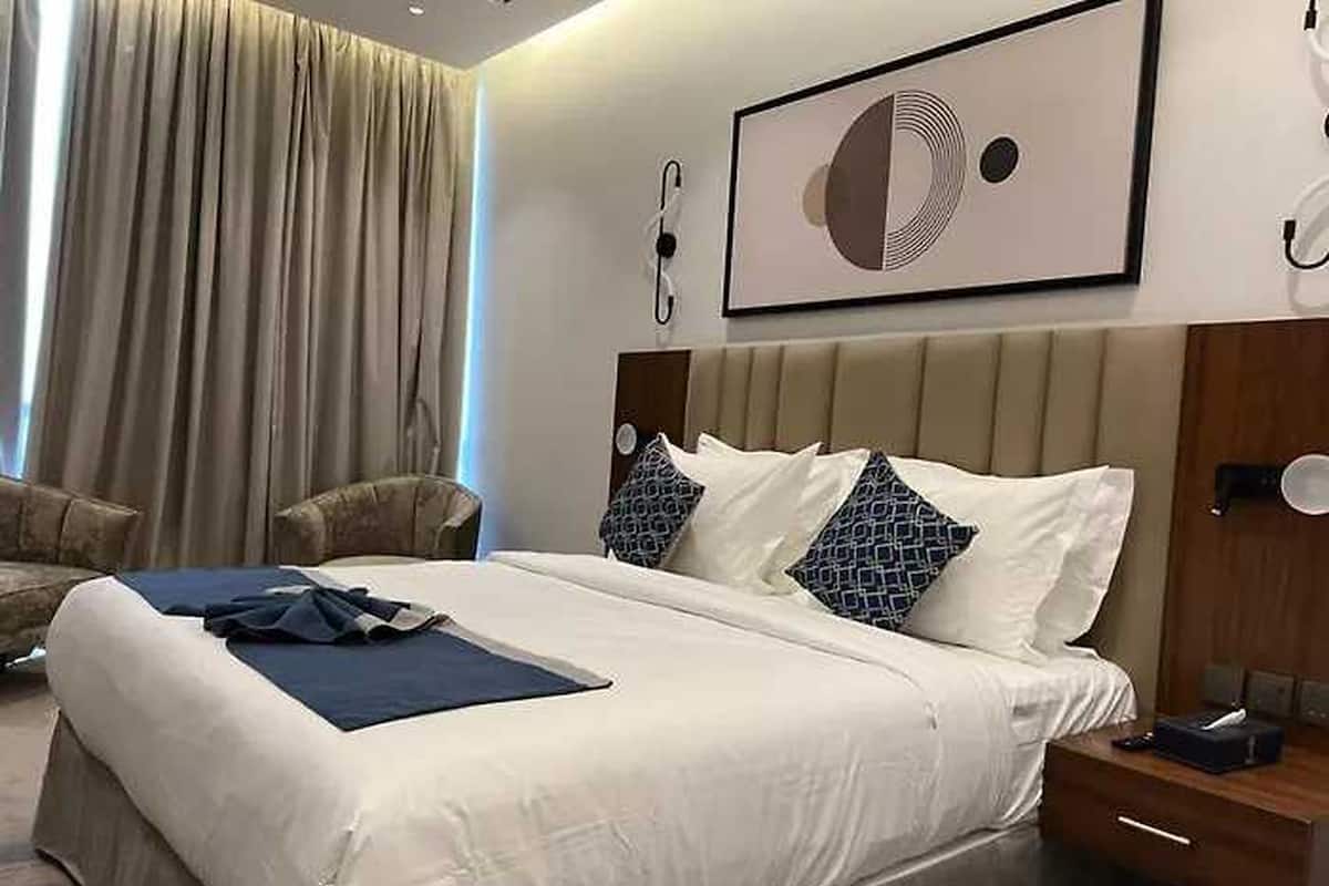 A hotel room with a large bed, a headboard, a bedside table, a chair, and a window with curtains.