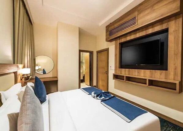 Hotellihuone, jossa on sänky, seinälle asennettu televisio, yöpöytä lampun kanssa ja peili.