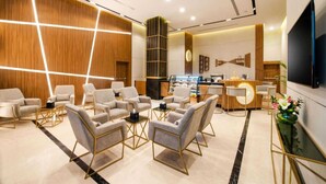 Eine moderne Hotelhalle mit Sitzgelegenheit, einer Rezeption und einem großen Flachbildfernseher.