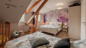 A bedroom with a sloped ceiling, a bed with floral bedding, a nightstand with a lamp, and a wardrobe.