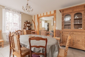 Uma sala de jantar com mesa redonda, cadeiras de madeira, um candelabro e um armário de madeira com portas de vidro.