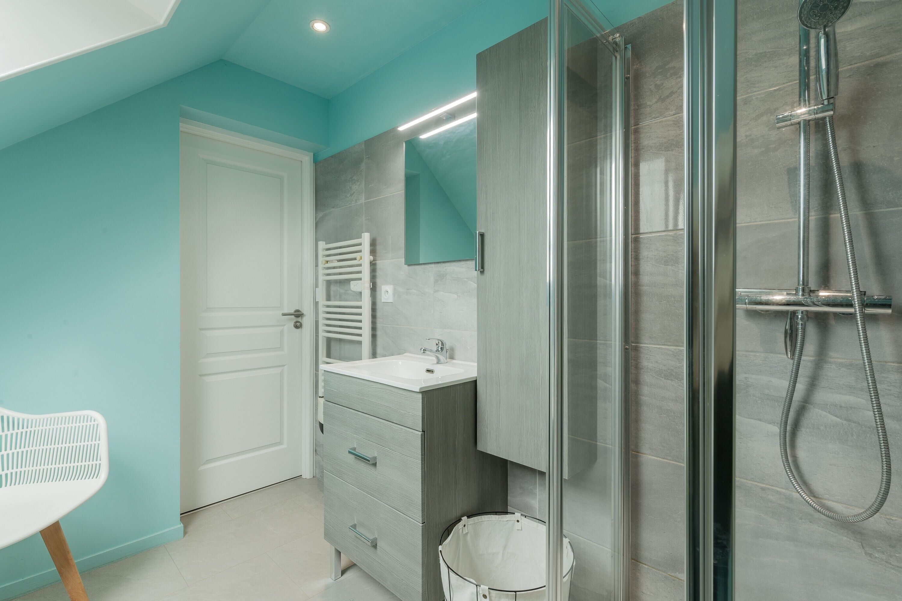 Een moderne badkamer met een douchecabine van glas, een witte wastafel en een witte stoel.