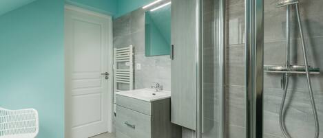Een moderne badkamer met een douchecabine van glas, een witte wastafel en een witte stoel.
