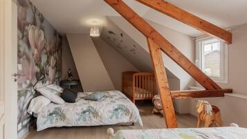 Une chambre avec un plafond en pente, un berceau, un cheval à bascule et un mur orné d’une fresque florale.