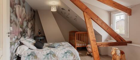 A bedroom with a sloped ceiling, a crib, a rocking horse, and a wall with a floral mural.