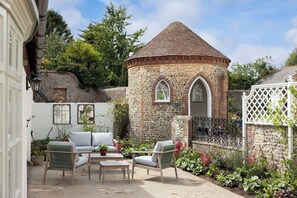 A stone tower with arched windows, surrounded by a garden with various plants and a white fence. - A modern 2 bedroom cottage located close to Arundel and Litthampton (Lyminster)