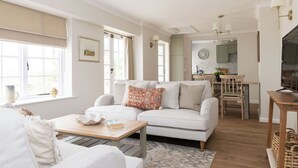 Una sala de estar moderna con un sofá blanco, una mesa de centro de madera y un comedor con una mesa y sillas de madera.